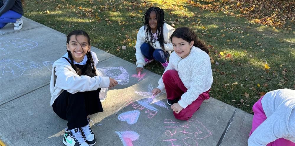  Students writing messages of kindness with chalk on the sidewalk.